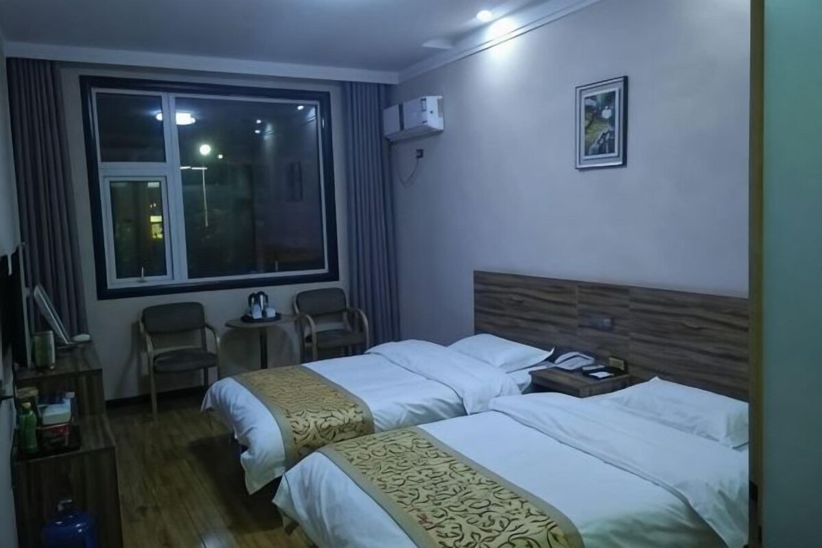 Habitación de hotel con dos camas, una ventana, una mesita y una silla.