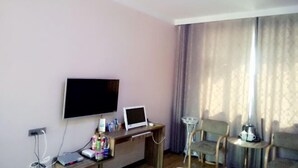 A hotel room with a flat-screen TV, a small desk with a computer, a chair, and a sofa. - Xinye Jinchen Business Hotel (Xinye)