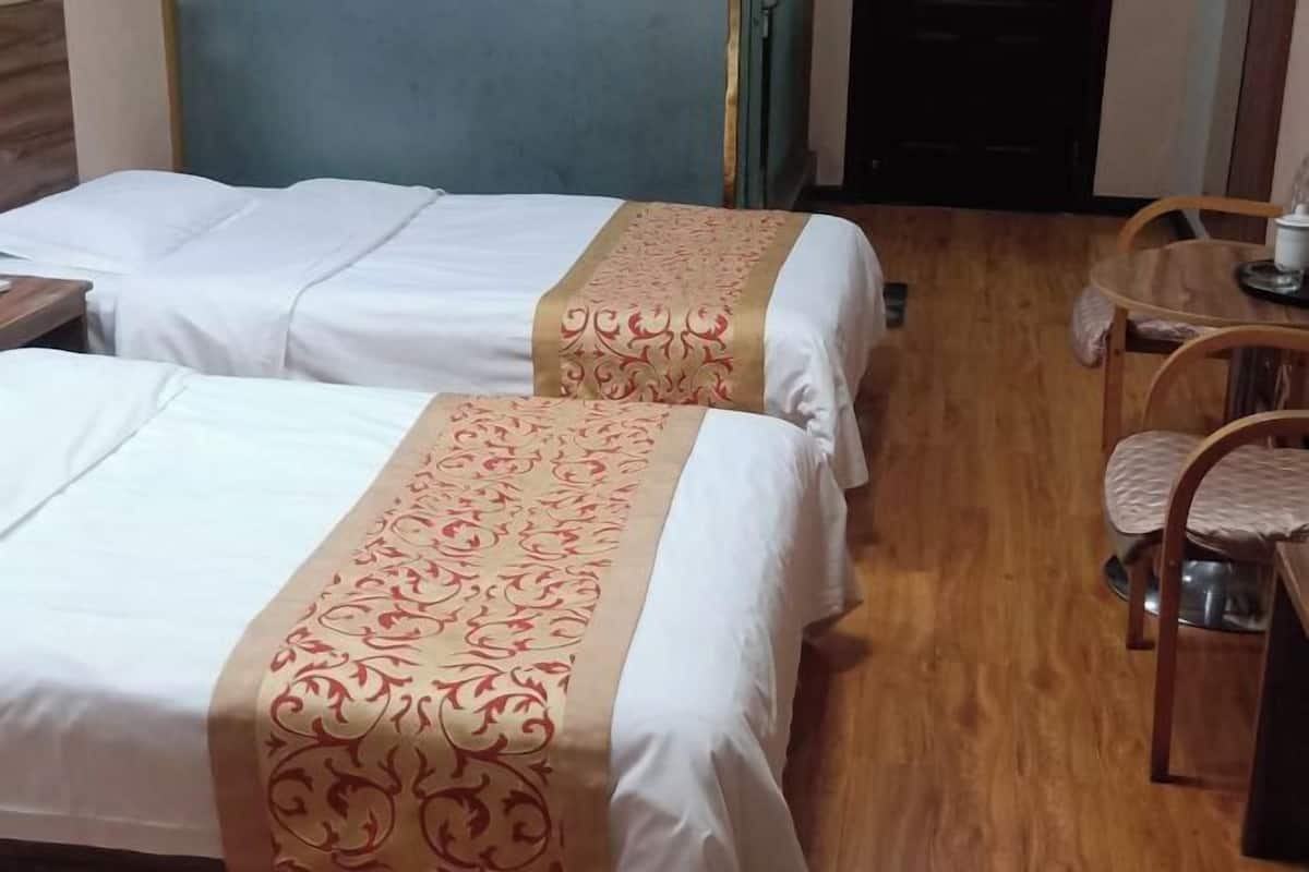 A hotel room with two beds, a wooden floor, a small table with chairs, and a door in the background.