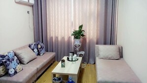 A living room with a sofa, a coffee table, a potted plant, and a curtain. - Xinye Jinchen Business Hotel (Xinye)