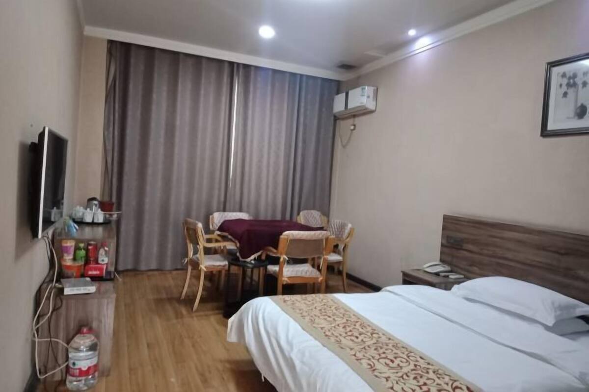 A hotel room with a bed, a desk with chairs, a television, and an air conditioning unit.