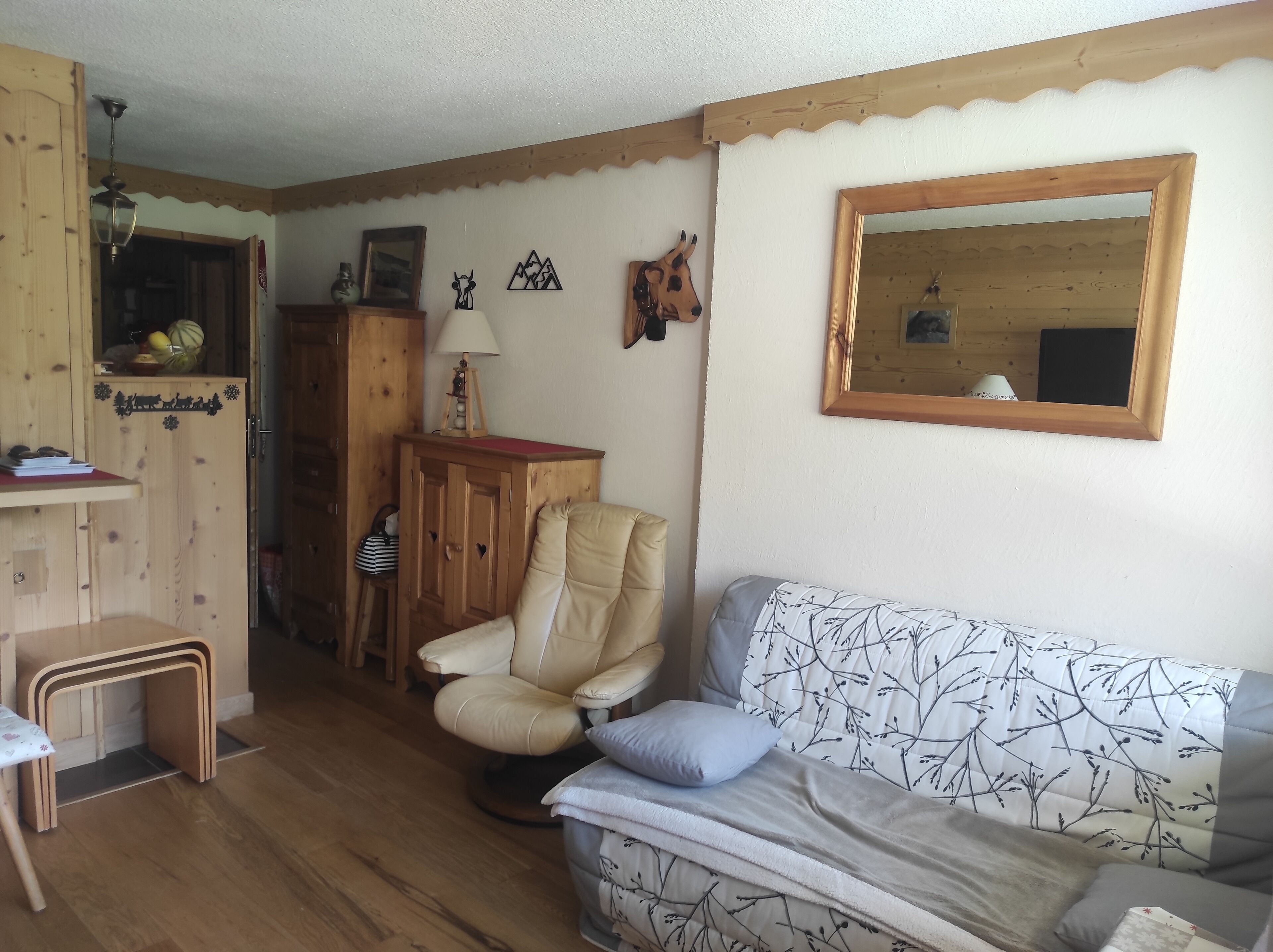 Een gezellige woonkamer met een houten kast, een fauteuil, een bank en een spiegel aan de muur.