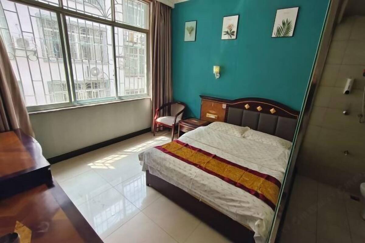 Een slaapkamer met een bed, een stoel, een bureau, een raam met tralies en een wand in een turquoise kleur.