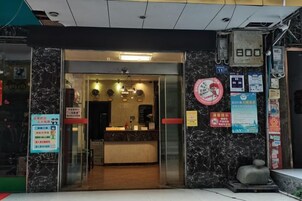 Entrada de un hotel con mostrador de recepción, pared de mármol y varios avisos.