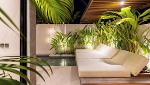 A modern outdoor seating area with a pool, surrounded by lush tropical plants and a wooden ceiling structure.