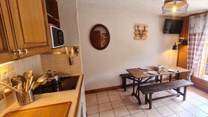 A kitchen with wooden cabinets, a microwave, a sink, and a dining table set for two with a bench. - Charming, well-equipped 4/6 pers Apt (Les Deux Alpes)