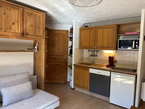Une cuisine compacte dotée d’armoires en bois, d’un four à micro-ondes, d’un évier et d’un réfrigérateur.