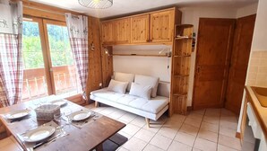 A cozy room with a wooden dining table set for two, a sofa, and wooden cabinets. - Charming, well-equipped 4/6 pers Apt (Les Deux Alpes)