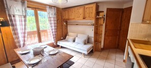 A cozy room with a wooden dining table set for two, a sofa, and wooden cabinets. - Charming, well-equipped 4/6 pers Apt (Les Deux Alpes)