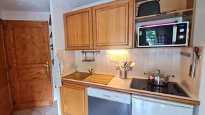 A compact kitchen with wooden cabinets, a microwave, a sink, a stove, and a dishwasher. - Charming, well-equipped 4/6 pers Apt (Les Deux Alpes)