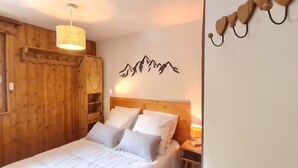 A wooden room with a bed, a hanging light fixture, and a wall decoration of mountains. - Charming, well-equipped 4/6 pers Apt (Les Deux Alpes)