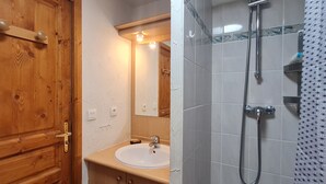 Ein Badezimmer mit Holztür, Waschbecken, Spiegel und Duschbereich.