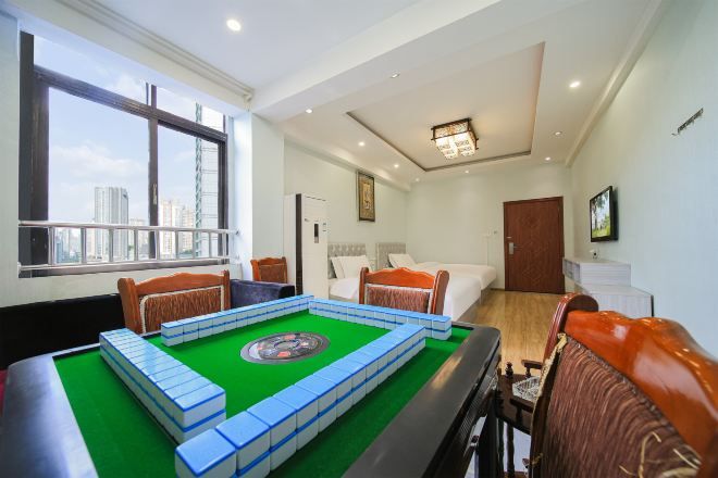 A hotel room with a pool table, a bed, a window with a city view, and a door.