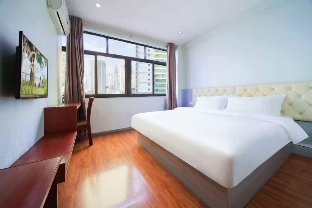 Une chambre d’hôtel équipée d’un lit, d’un bureau, d’une chaise, d’une télévision et d’une fenêtre donnant sur la ville.