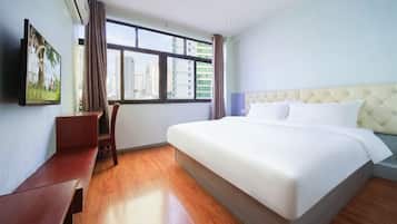A hotel room with a bed, a desk, a chair, a TV, and a window with a city view.