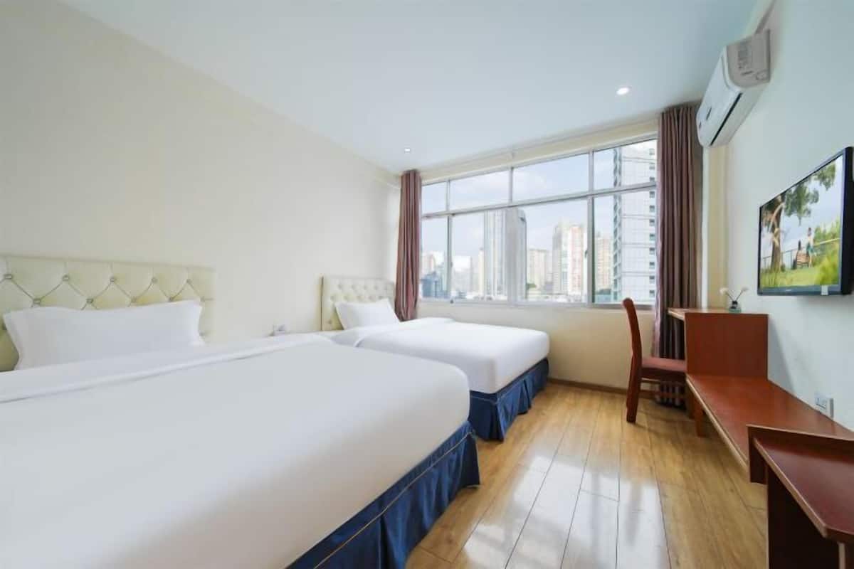Une chambre d’hôtel avec deux lits, un bureau, une chaise et une grande fenêtre donnant sur la ville.