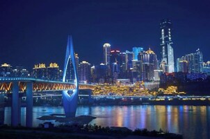 Un horizonte urbano nocturno con edificios iluminados, un puente destacado y una masa de agua que refleja las luces.