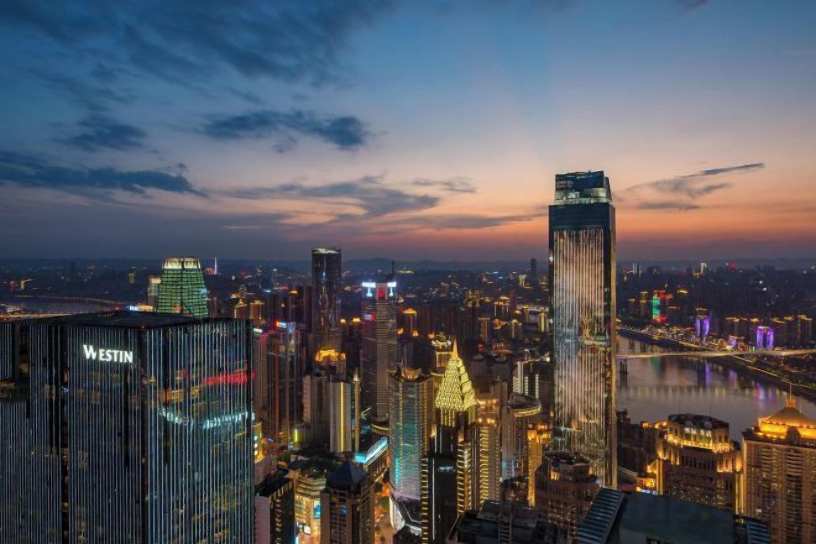 Une vue sur une ville au crépuscule, avec des bâtiments illuminés et une rivière.