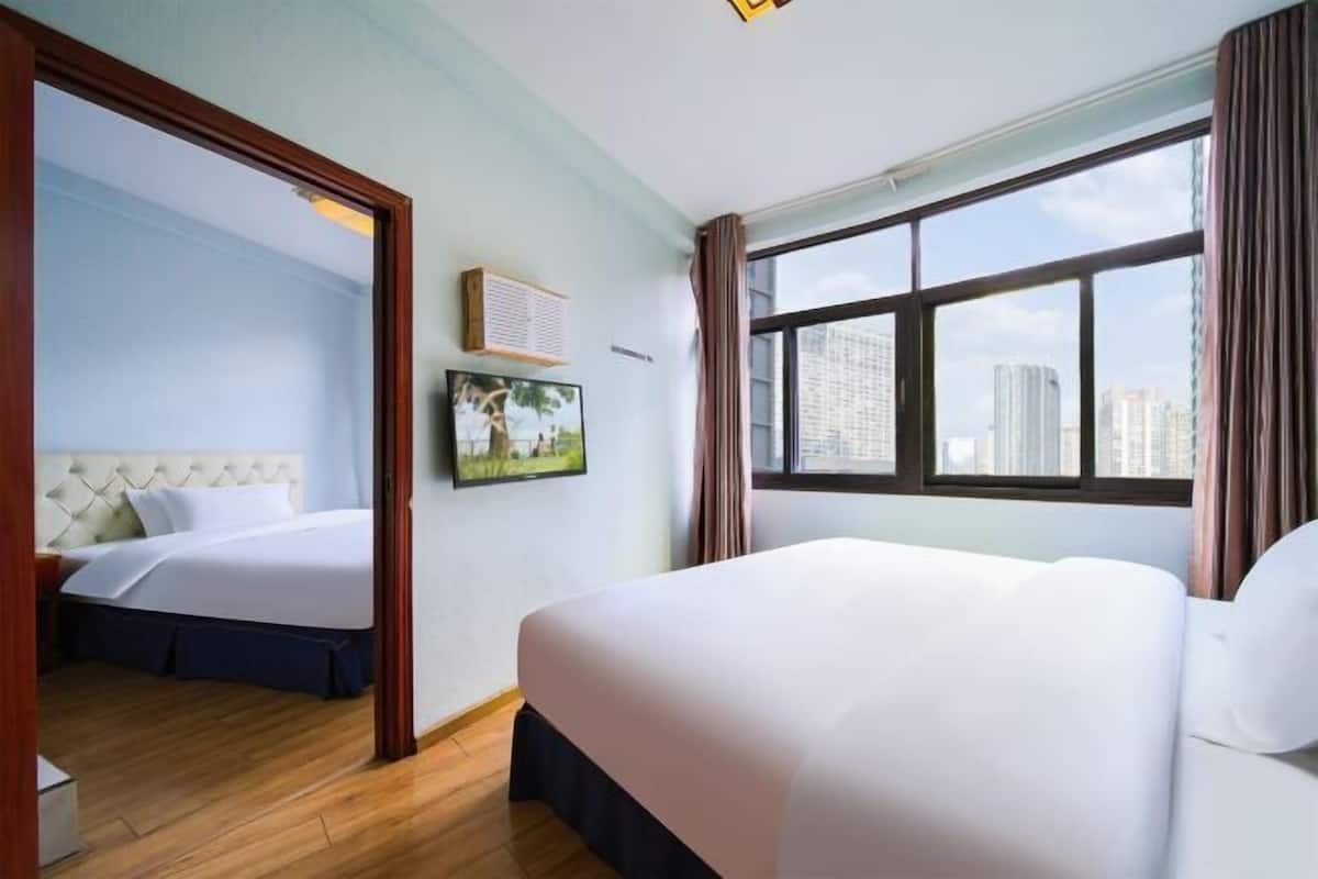 Une chambre d’hôtel avec un grand lit, un plus petit lit, une fenêtre donnant sur la ville, un miroir et un tableau au mur.