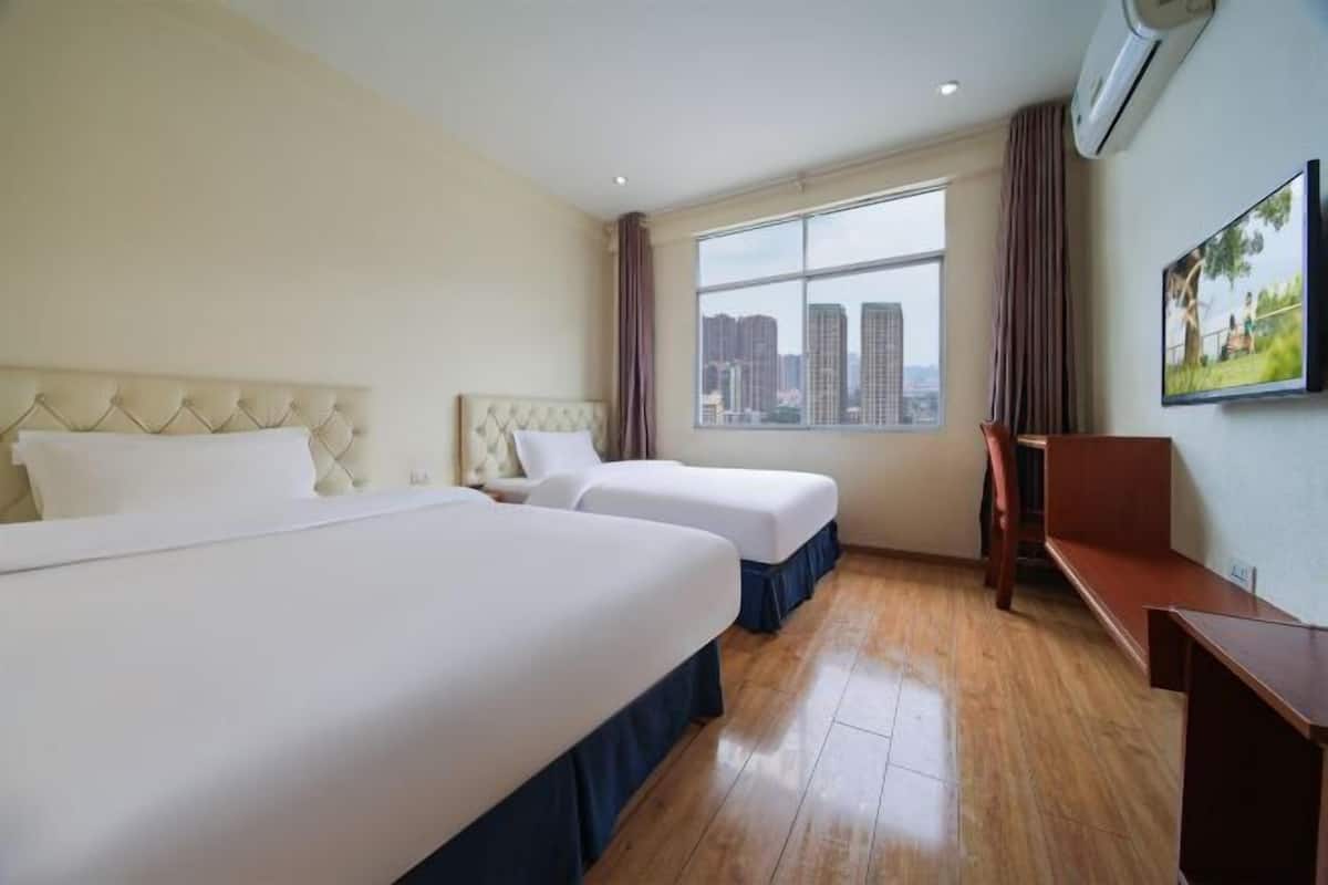 Une chambre d’hôtel avec deux lits, un bureau, une chaise, une grande fenêtre donnant sur la ville et un appareil de climatisation.