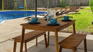 Una mesa de madera con bancos y un paraguas amarillo en un patio con piscina.