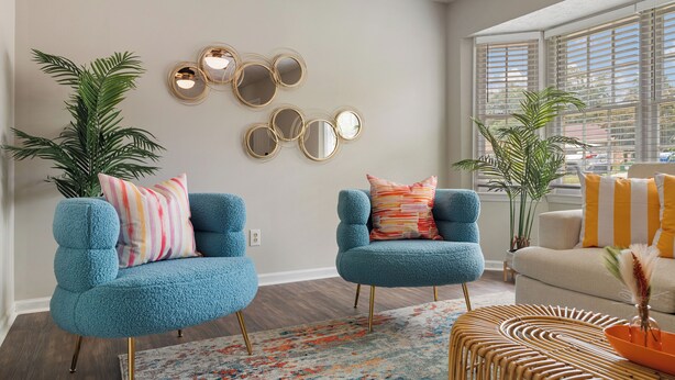 Una sala de estar con dos sillones azules, un sofá color beige, un tapete estampado y un conjunto de espejos montados en la pared.