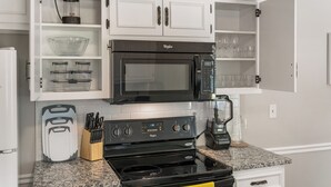 Una cocina con armarios blancos, microondas negro, estufa y licuadora.