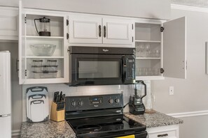 A kitchen with white cabinets, a black microwave, a stove, and a blender.