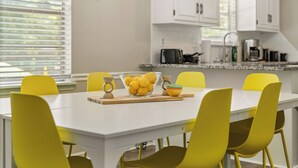 Una cocina luminosa con armarios blancos, encimera blanca y sillas amarillas alrededor de una mesa central con un bol de limones.