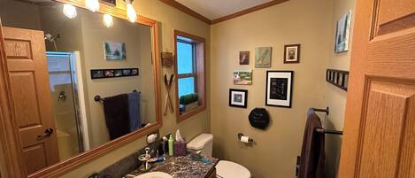 A bathroom with a sink, toilet, and mirror. There are framed pictures on the wall and a window with a view of the outside.