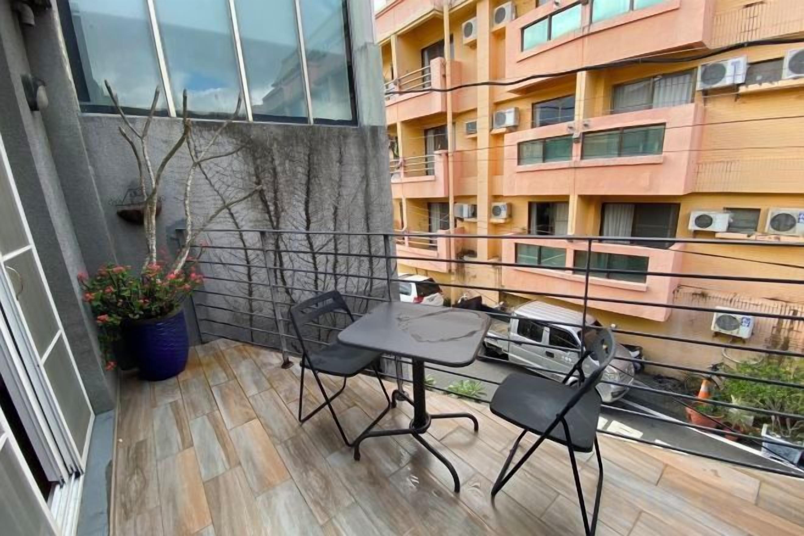 A balcony with a table and chairs, a potted plant, and a view of a multi-story building with balconies.