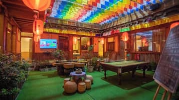 A room with a pool table, green artificial turf, and a colorful ceiling.