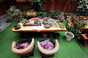 Une table en bois, agrémentée de plantes en pot et surmontée d’une petite armoire en bois, le tout entouré de chaises en osier dotées de coussins.
