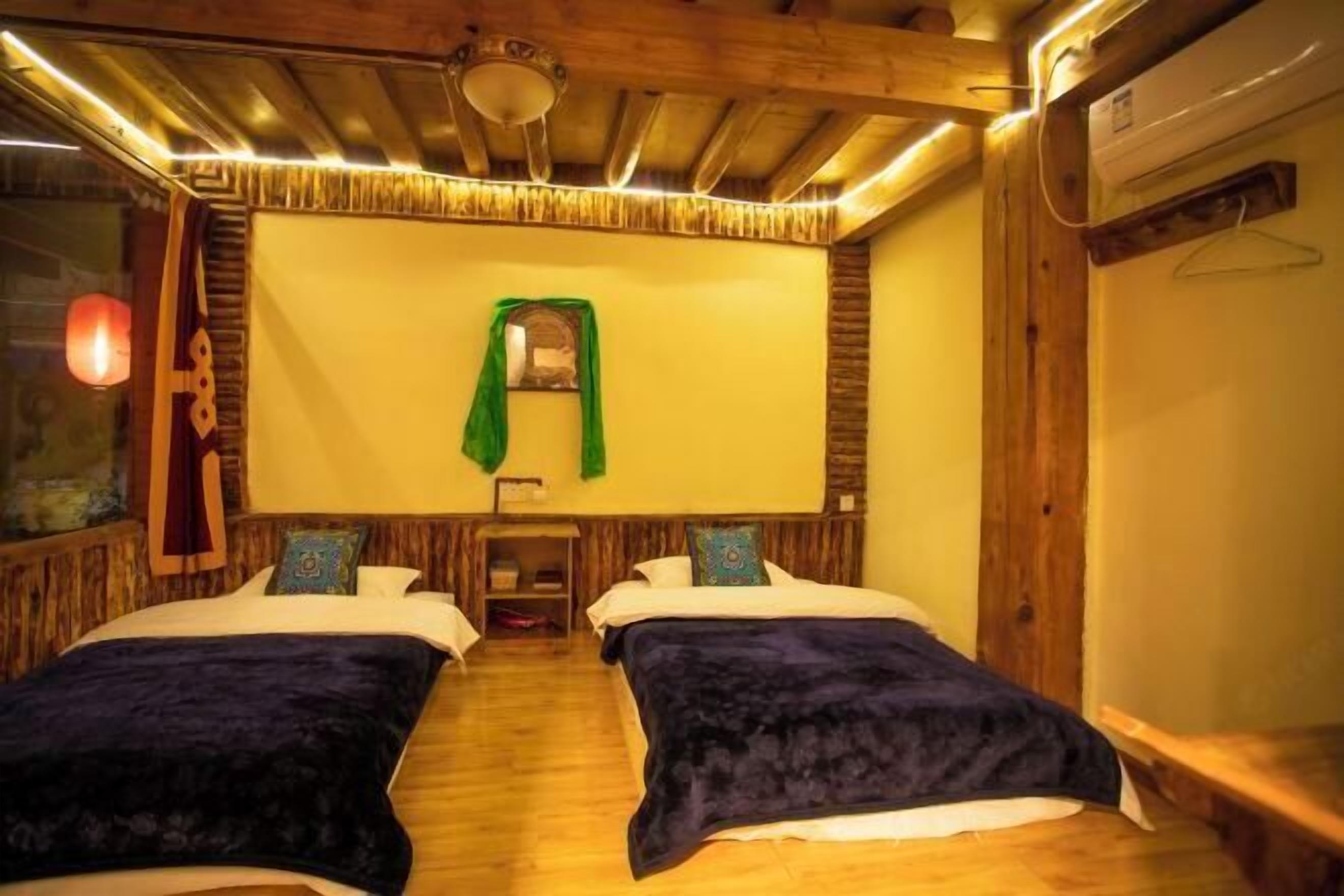 A room with two beds, wooden beams on the ceiling, a hanging green garment, and a small shelf with items.