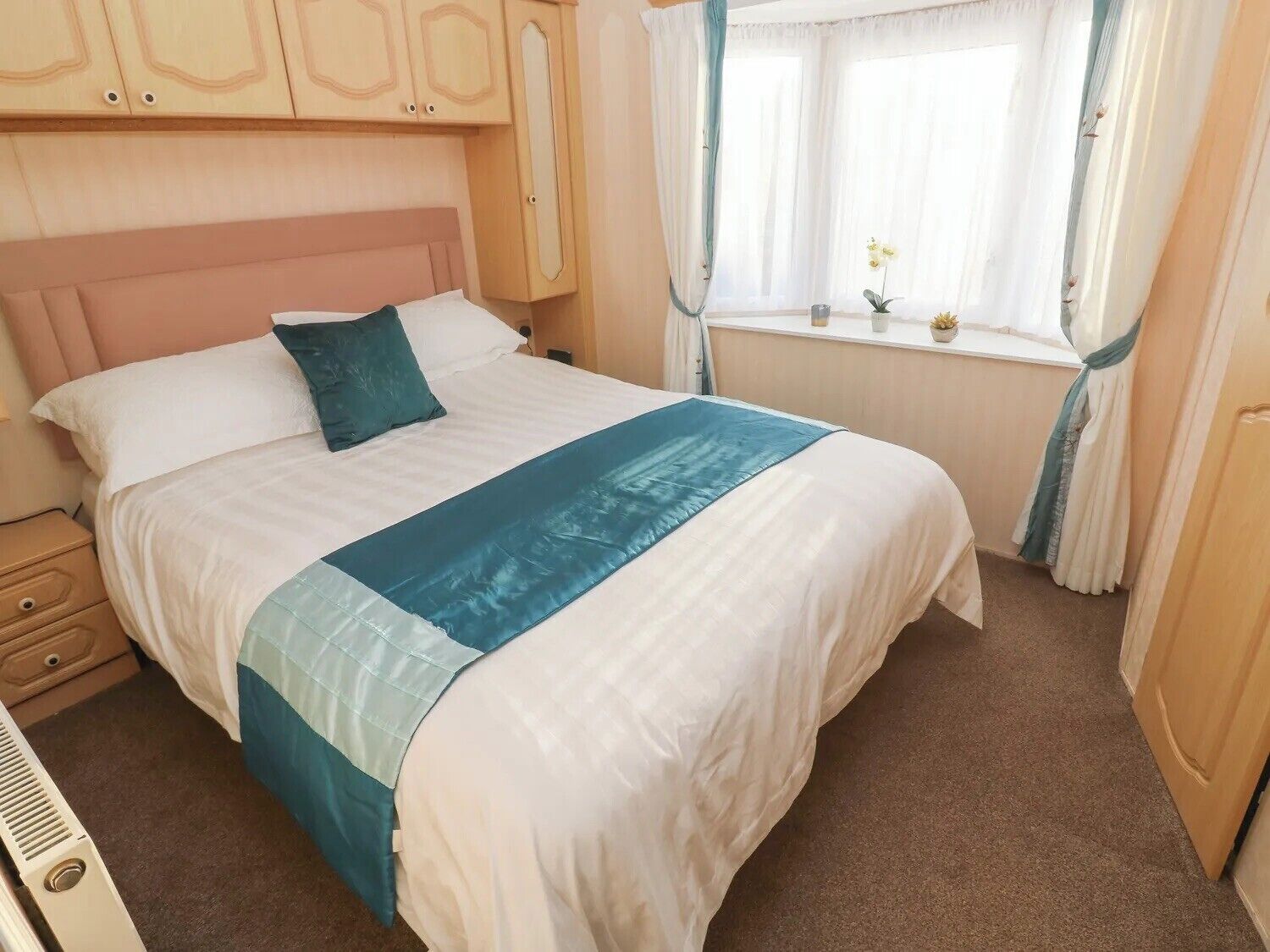 A neatly made bed with a blue accent, a wooden headboard, a bedside table, and a window with curtains.