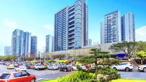 A busy urban street with tall modern buildings, a parking lot, and greenery. - Hotel & Davos (Chongqing Ranjiaba Light Rail Station) (Chongqing)