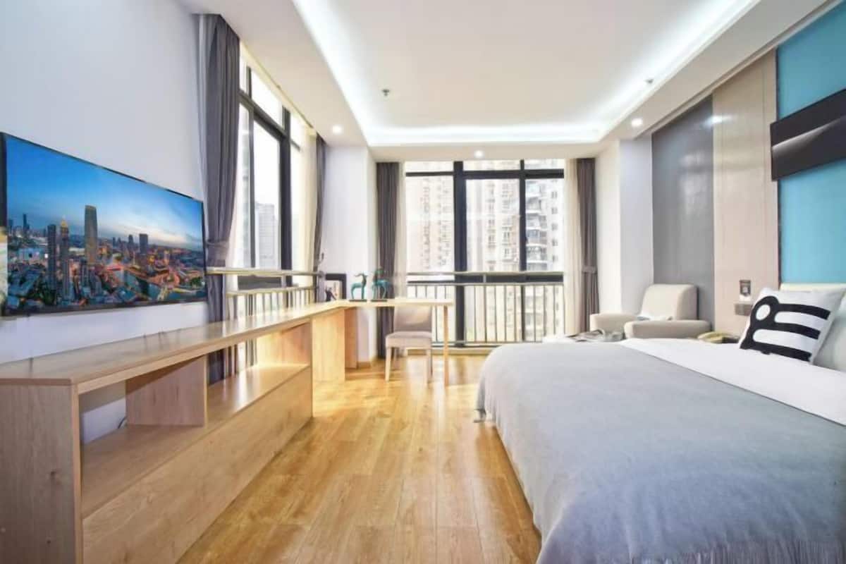 A modern hotel room with a large bed, a desk, and a balcony with a city view.