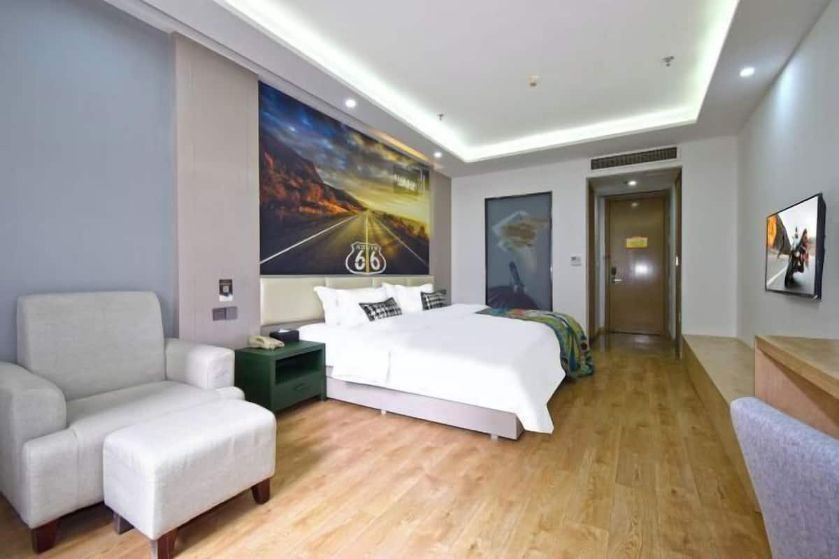 A modern hotel room with a large bed, a sofa, a nightstand, and a wall with a poster.