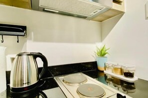 A modern kitchen with a stainless steel kettle, a stove, and a small potted plant. - Gavin's Place @ FAME Residences (Mandaluyong)