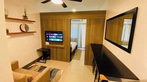 Una habitación de hotel moderna con televisión de pantalla plana, ventilador de techo, cama y escritorio con silla.
