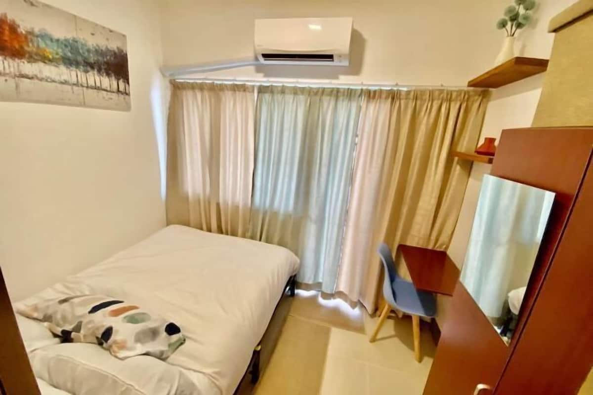 A room with a bed, an air conditioner, a chair, and a wardrobe.