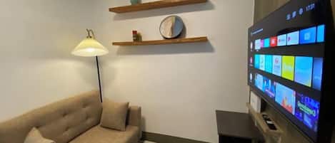 A living room with a sofa, a lamp, a flat-screen TV, and wooden shelves.