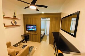 A modern living room with a flat-screen TV, a ceiling fan, a sofa, and a dining area. - Gavin's Place @ FAME Residences (Mandaluyong)