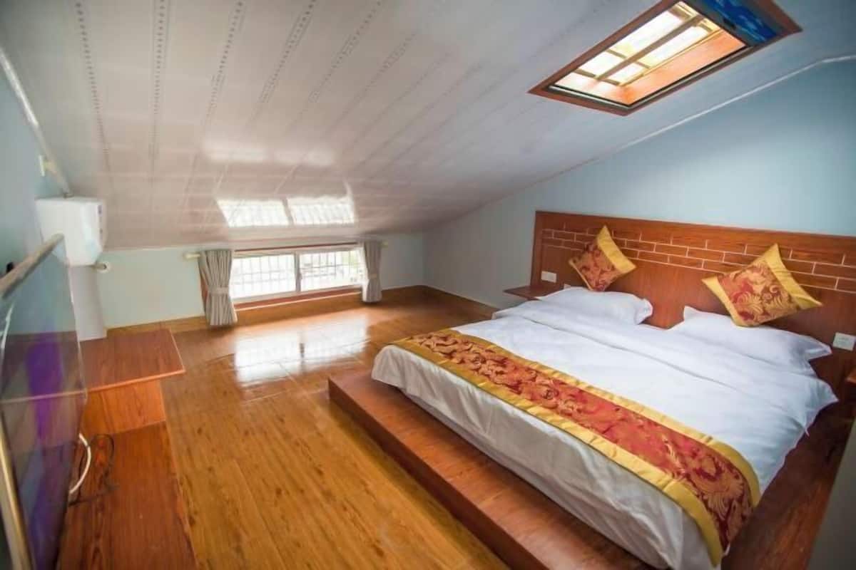 A bedroom with a wooden floor, a bed with a white and red bedspread, a wooden headboard, and a skylight.