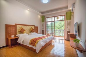 Una camera da letto con un letto grande, una testiera in legno, comodini, una TV e un balcone con vista sul verde.