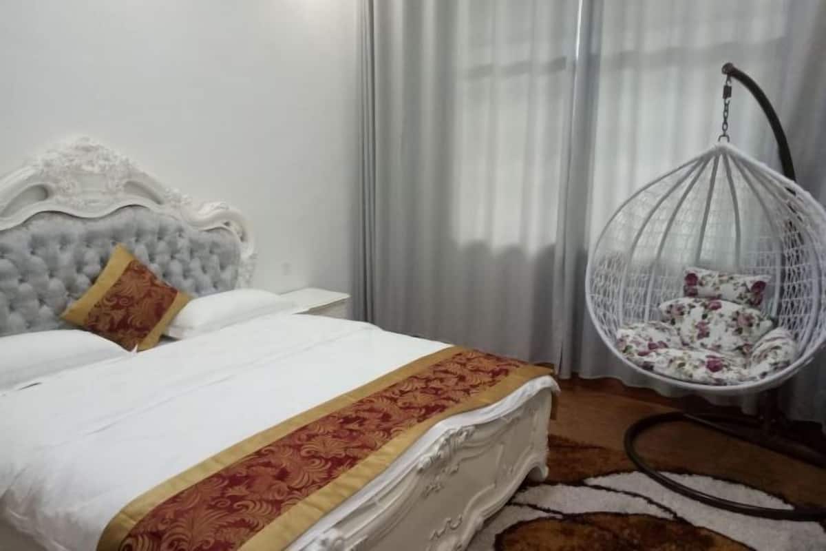 A bed with a white headboard, a hanging chair with a floral pattern, and a patterned rug on the floor.