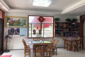 A dining area with round tables and chairs, a window with decorative elements, and a bookshelf with various items. - Haolaiju Inn (Zhangjiajie)
