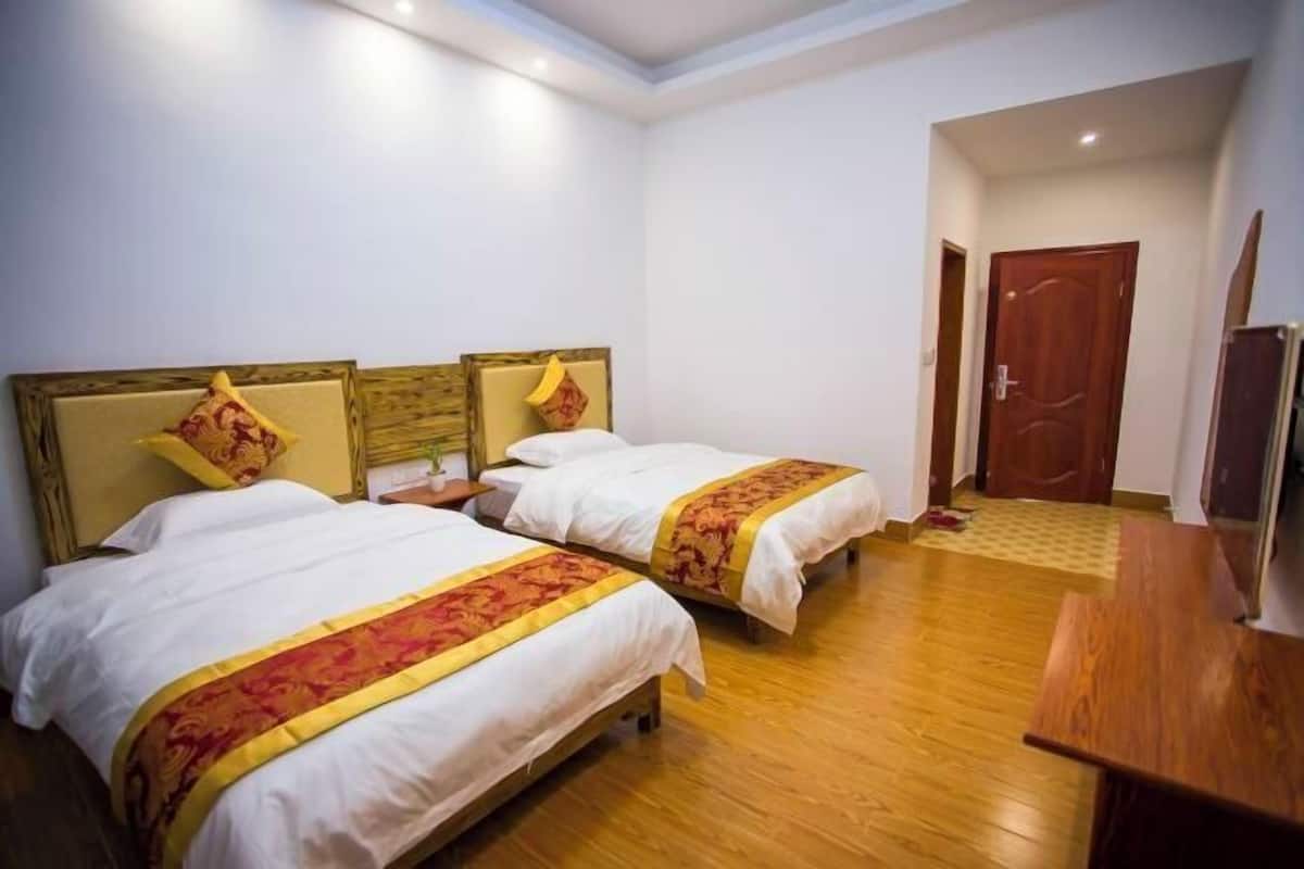 A hotel room with two beds, wooden floors, a wooden door, and a small desk.