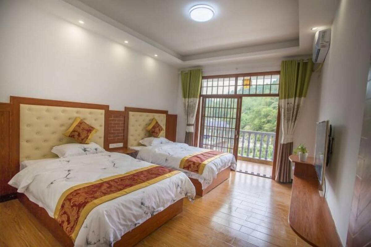 A hotel room with two beds, a balcony with a view, and a TV on the wall.