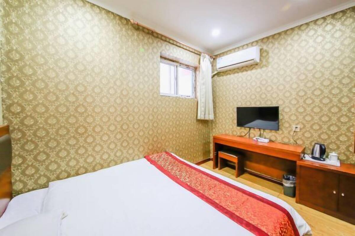 A hotel room with a bed, a TV, a desk, and an air conditioning unit.